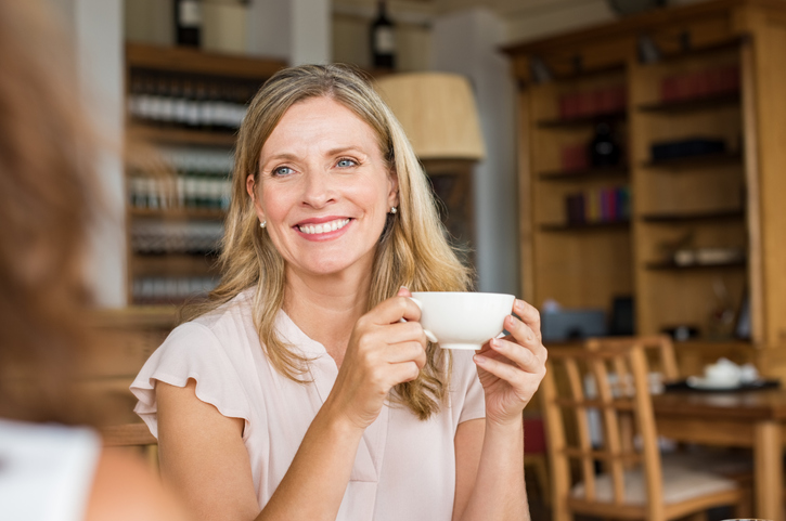 A middle-aged woman smiling and holding a tea cup.