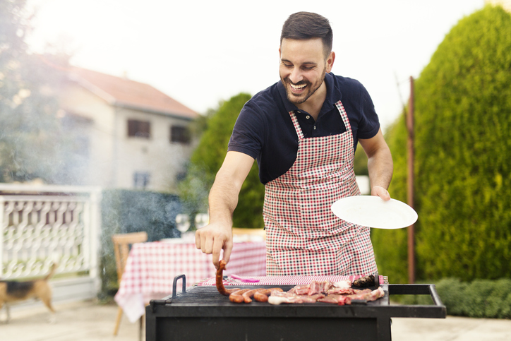 Young man in an apron grilling sausages.