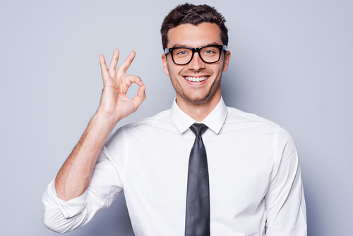 Happy young man in shirt and tie gesturing OK sign and smiling