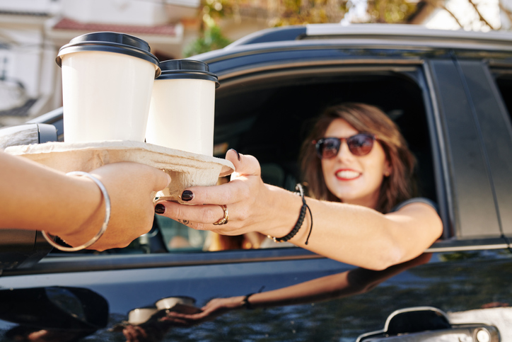 A woman giving another woman in a car a drink tray with two coffees.