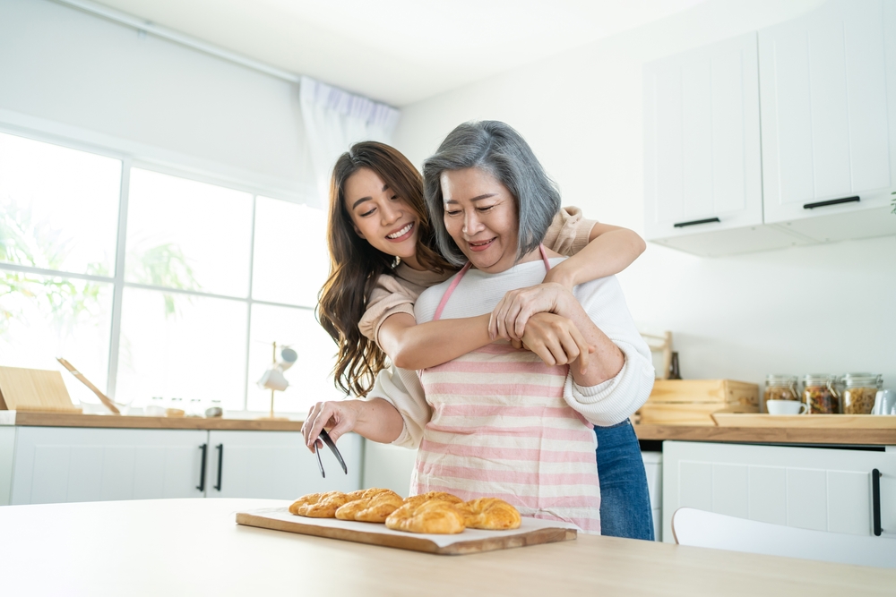 A grandmother and adult granddaughter hug while baking croissants